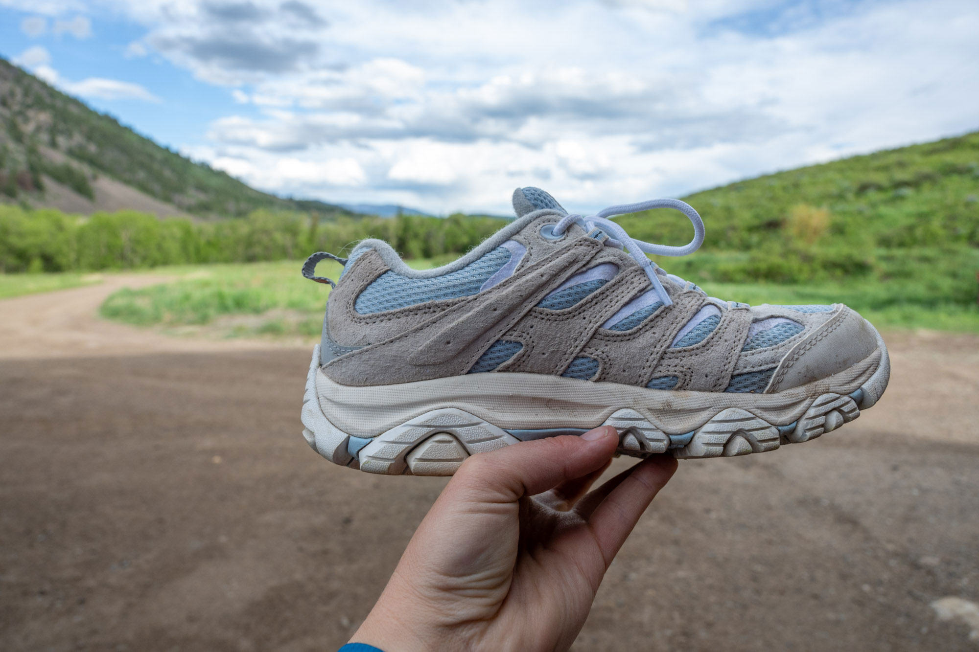 A hand holding Merrell Moab 3 hiking shoe