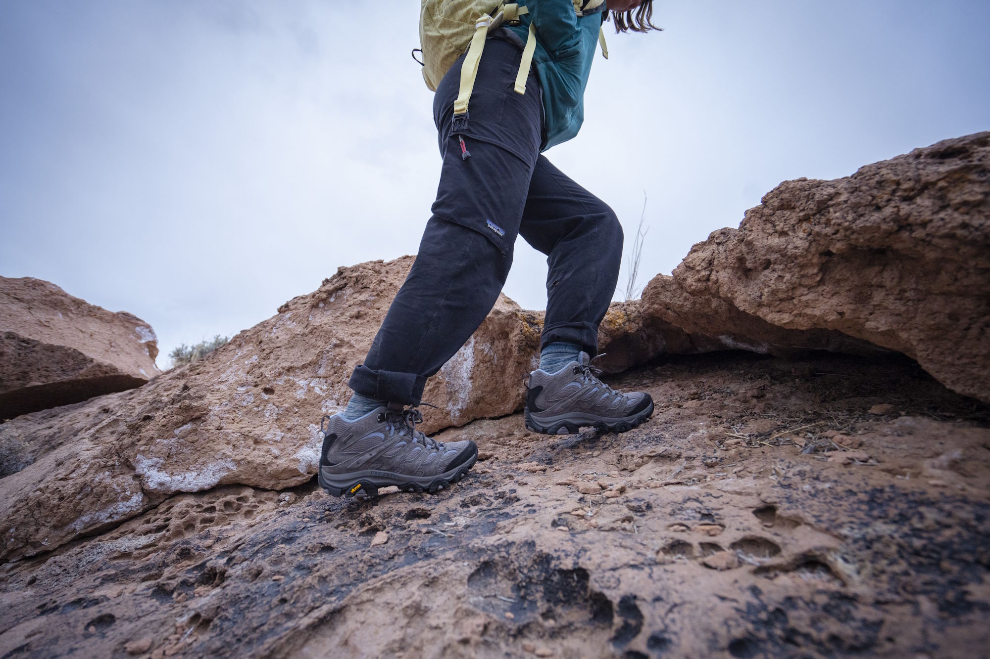 A person wearing moab 3 hiking boots and a backpack climbs over rocky terrain